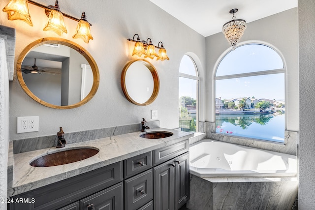 bathroom with vanity, ceiling fan with notable chandelier, tiled tub, and a water view