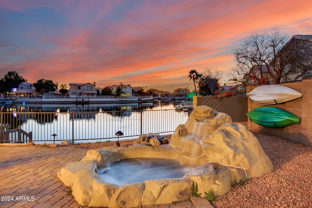 pool at dusk with a hot tub and a water view