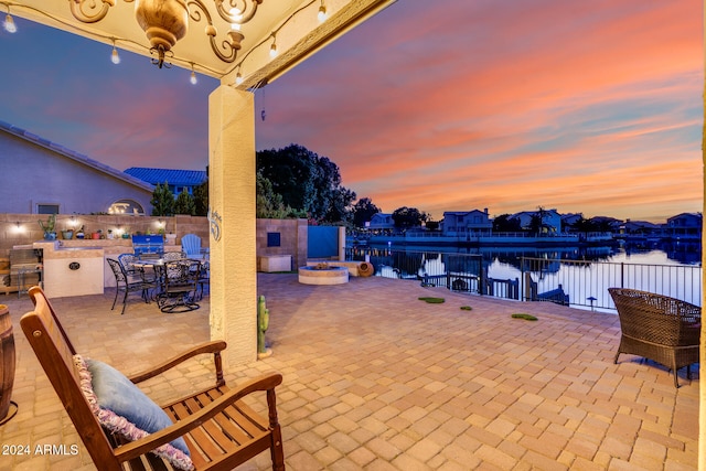 patio terrace at dusk featuring a water view, a hot tub, and exterior kitchen