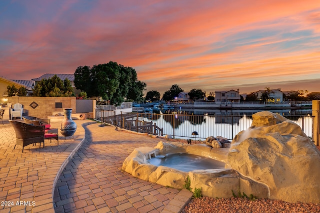 pool at dusk with a patio area and a water view