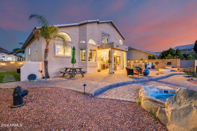 back house at dusk featuring an in ground hot tub and a patio