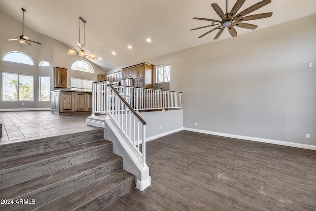 staircase with high vaulted ceiling, ceiling fan with notable chandelier, hardwood / wood-style flooring, and a healthy amount of sunlight