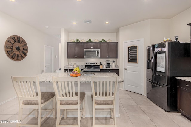 kitchen with appliances with stainless steel finishes, a kitchen island with sink, light tile patterned floors, and dark brown cabinetry