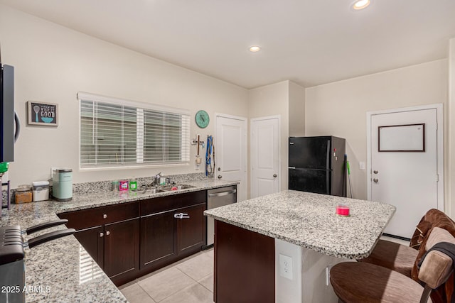 kitchen featuring sink, black refrigerator, a kitchen island, light stone countertops, and a kitchen bar