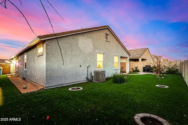 back house at dusk featuring a lawn, central AC unit, and an outdoor fire pit