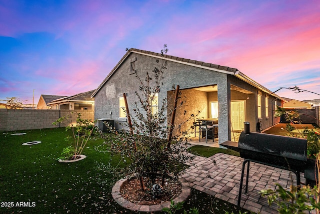 back house at dusk featuring a patio, a yard, and cooling unit