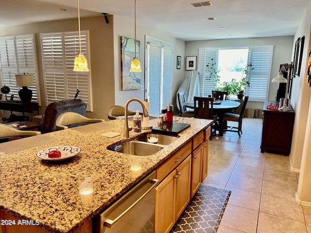 kitchen featuring an island with sink, sink, stainless steel dishwasher, decorative light fixtures, and light stone countertops