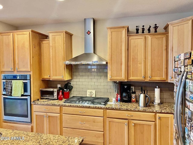 kitchen with light stone countertops, stainless steel appliances, tasteful backsplash, and wall chimney range hood