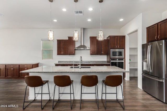 kitchen featuring sink, wall chimney exhaust hood, an island with sink, decorative light fixtures, and appliances with stainless steel finishes