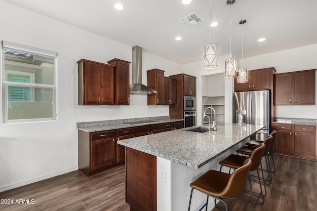 kitchen featuring light stone countertops, stainless steel appliances, a kitchen island with sink, wall chimney range hood, and pendant lighting