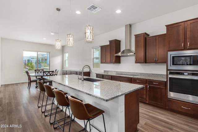 kitchen with a center island with sink, sink, appliances with stainless steel finishes, decorative light fixtures, and light stone counters