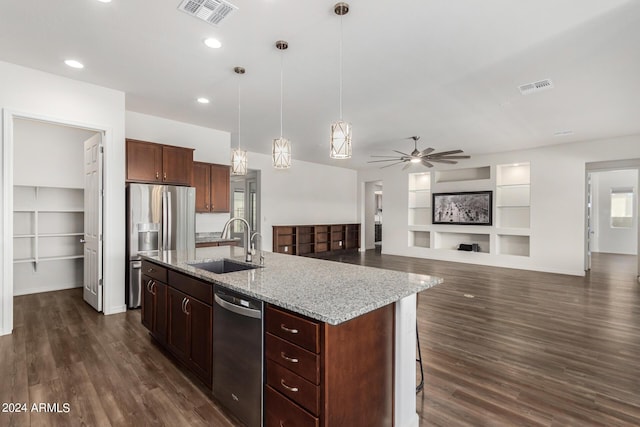 kitchen featuring built in shelves, stainless steel appliances, sink, pendant lighting, and an island with sink