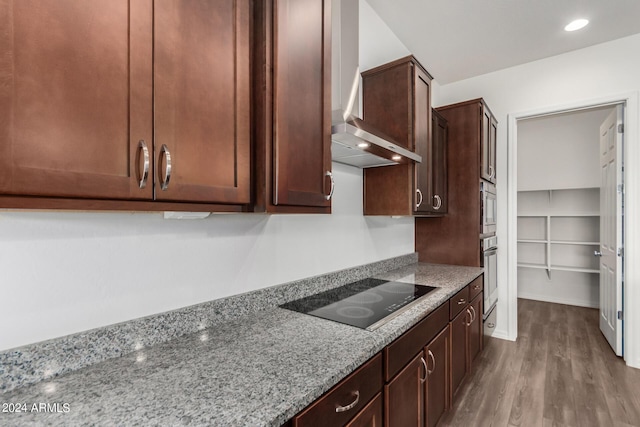 kitchen featuring light stone countertops, wall chimney exhaust hood, stainless steel oven, black electric cooktop, and hardwood / wood-style floors