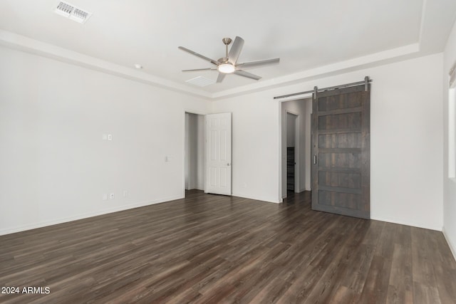 empty room featuring a barn door, a tray ceiling, ceiling fan, and dark wood-type flooring