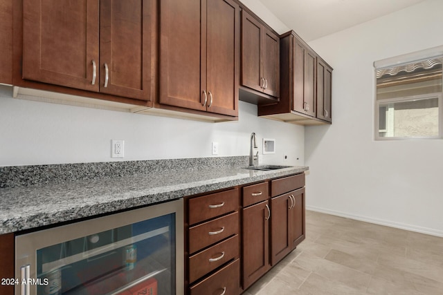 kitchen with dark brown cabinets, light stone counters, wine cooler, and sink