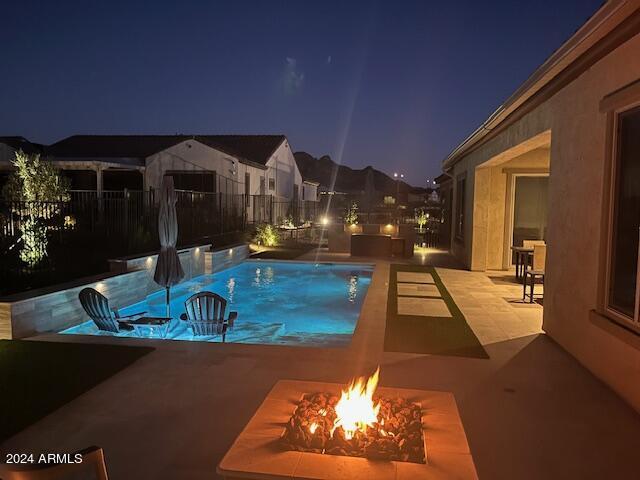 pool at twilight featuring pool water feature, a patio, and an outdoor fire pit