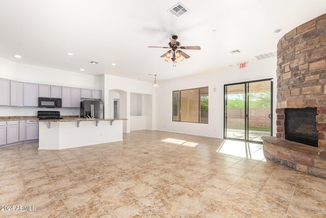 kitchen featuring a breakfast bar, a kitchen island with sink, black appliances, a stone fireplace, and ceiling fan