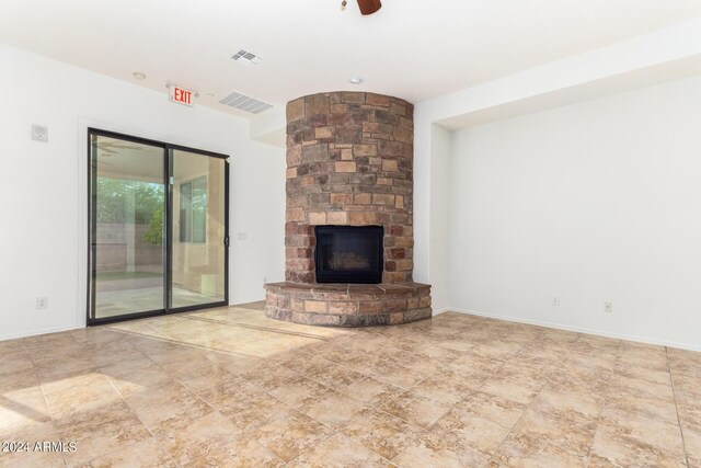 unfurnished living room with a stone fireplace and ceiling fan