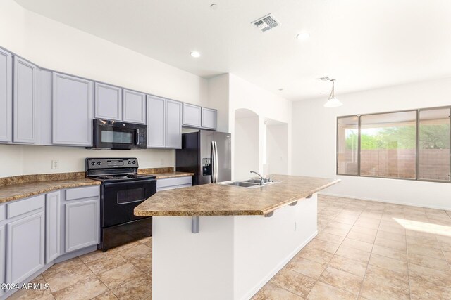 kitchen featuring a breakfast bar, pendant lighting, black appliances, a center island with sink, and sink