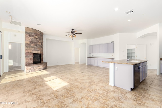 kitchen featuring dishwasher, sink, an island with sink, a large fireplace, and ceiling fan