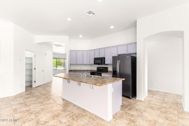 kitchen featuring sink, a center island with sink, black appliances, gray cabinets, and a breakfast bar