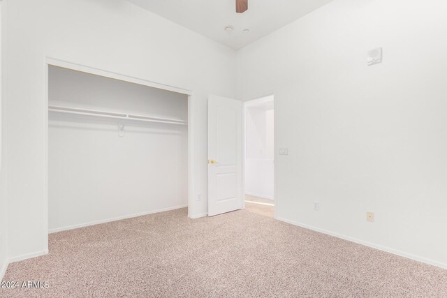 unfurnished bedroom featuring light carpet, a closet, a high ceiling, and ceiling fan