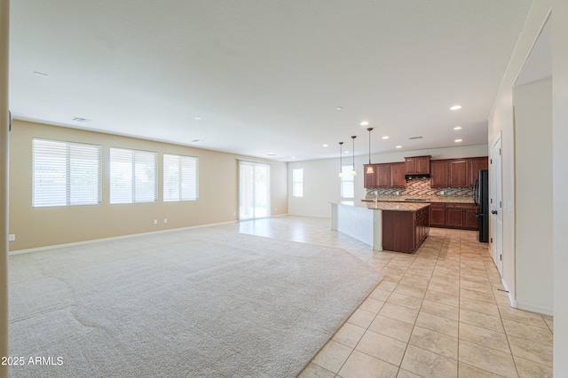 kitchen with open floor plan, light tile patterned floors, decorative backsplash, hanging light fixtures, and freestanding refrigerator