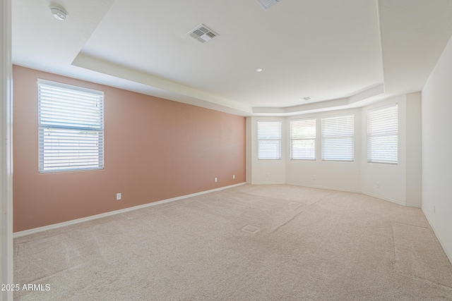 empty room featuring a wealth of natural light, visible vents, and a raised ceiling