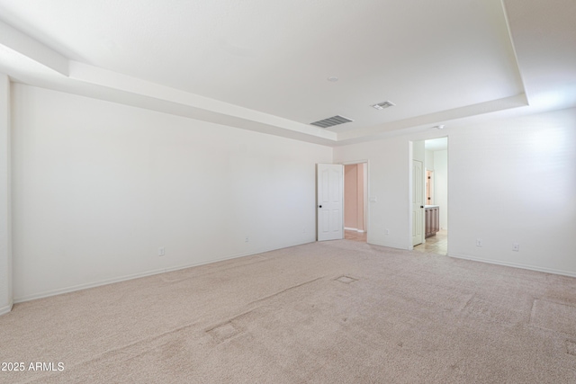 unfurnished room with a raised ceiling, light carpet, baseboards, and visible vents