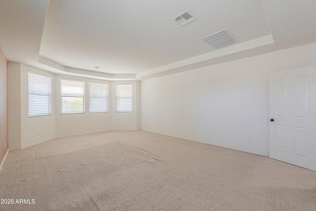 unfurnished room featuring a raised ceiling, light carpet, baseboards, and visible vents