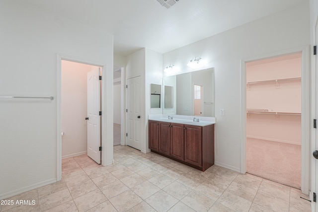 bathroom featuring baseboards, double vanity, tile patterned floors, a sink, and a spacious closet