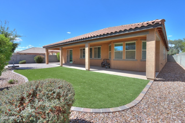 rear view of house with stucco siding, a fenced backyard, a tiled roof, a patio, and a lawn