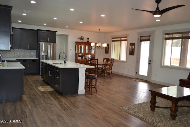 kitchen with a center island with sink, light countertops, hanging light fixtures, a sink, and stainless steel fridge with ice dispenser