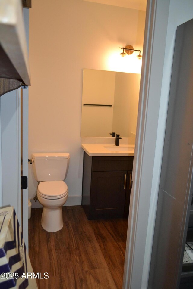 bathroom with toilet, baseboards, wood finished floors, and vanity