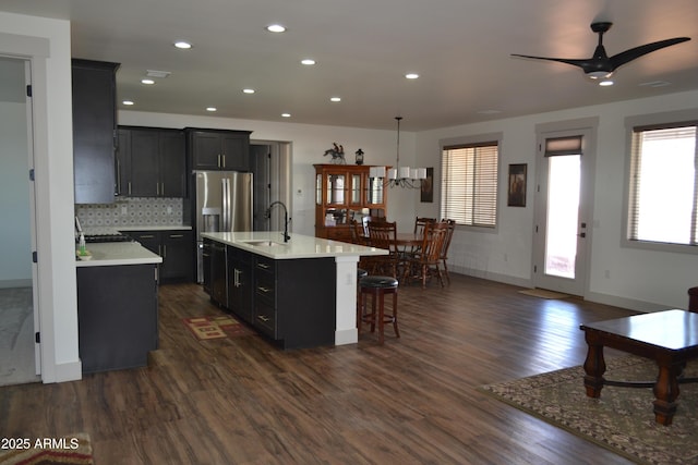 kitchen featuring light countertops, a sink, a kitchen island with sink, and dark cabinets