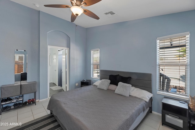 bedroom with ceiling fan, visible vents, light tile patterned floors, baseboards, and ensuite bathroom