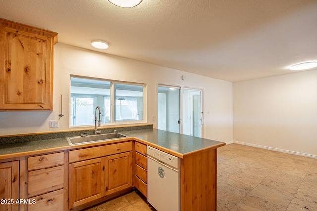 kitchen featuring a peninsula, a sink, baseboards, dishwasher, and dark countertops