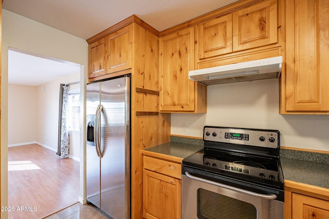 kitchen featuring light wood-style flooring, under cabinet range hood, baseboards, appliances with stainless steel finishes, and dark countertops