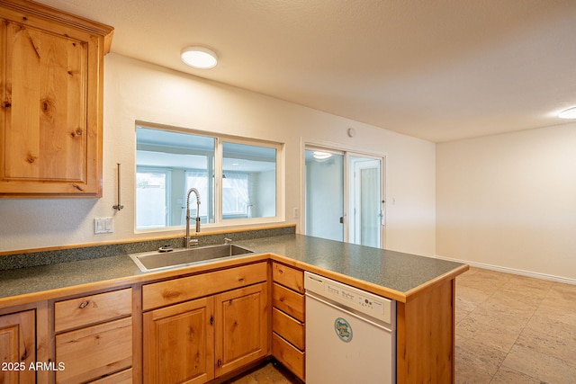 kitchen with dark countertops, dishwasher, a peninsula, and a sink