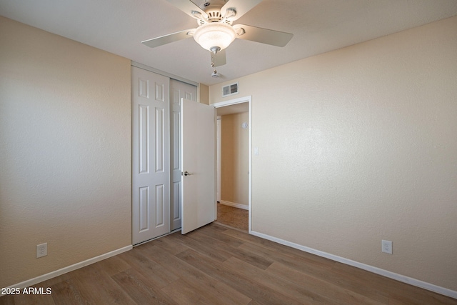 unfurnished bedroom with a closet, visible vents, baseboards, and wood finished floors