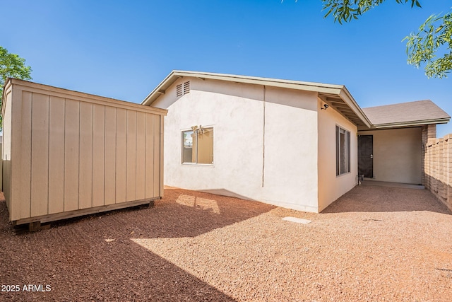 view of property exterior with stucco siding, a storage unit, and an outbuilding