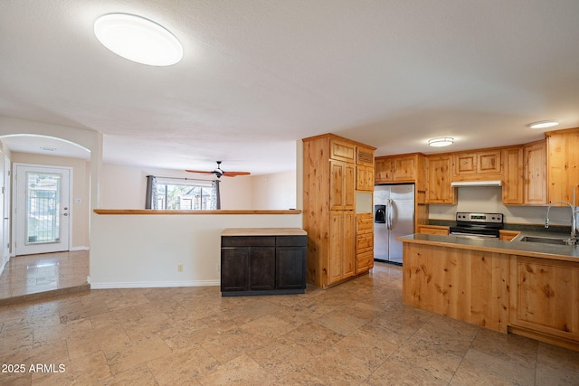 kitchen featuring stainless steel appliances, a sink, a ceiling fan, baseboards, and stone finish flooring