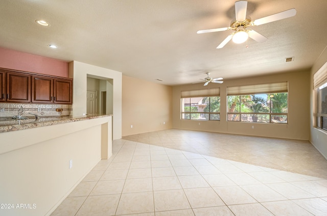 kitchen with light stone countertops, light tile patterned floors, tasteful backsplash, and ceiling fan