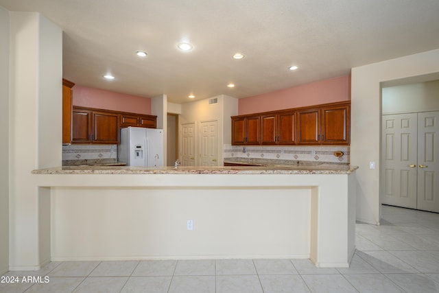 kitchen featuring white refrigerator with ice dispenser, decorative backsplash, light tile patterned flooring, light stone counters, and kitchen peninsula