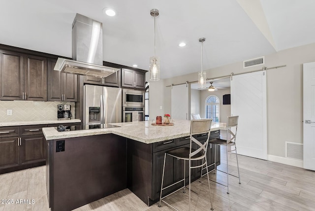 8361 E San Rafael Dr, Scottsdale, AZ 85258 - kitchen with appliances with stainless steel finishes, wall chimney range hood, a kitchen breakfast bar, a barn door, and a center island