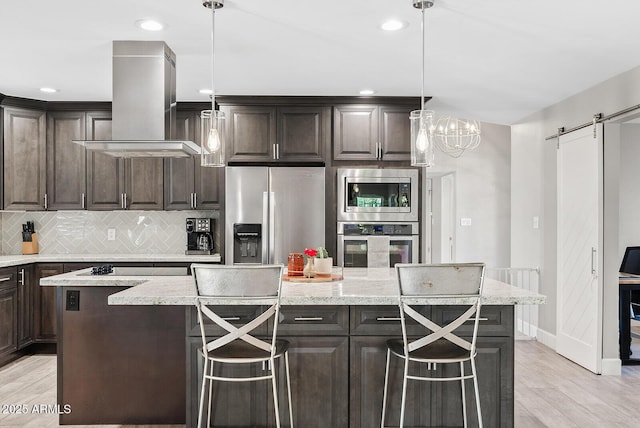 8361 E San Rafael Dr, Scottsdale, AZ 85258 - kitchen with appliances with stainless steel finishes, wall chimney exhaust hood, a barn door, dark brown cabinets, and a kitchen island