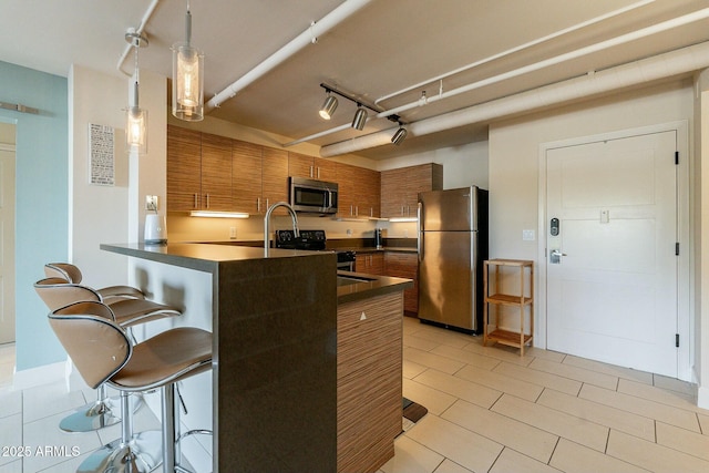 kitchen featuring rail lighting, a breakfast bar, decorative light fixtures, kitchen peninsula, and stainless steel appliances