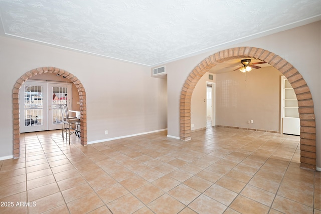 empty room with light tile patterned floors, visible vents, a textured ceiling, and a ceiling fan