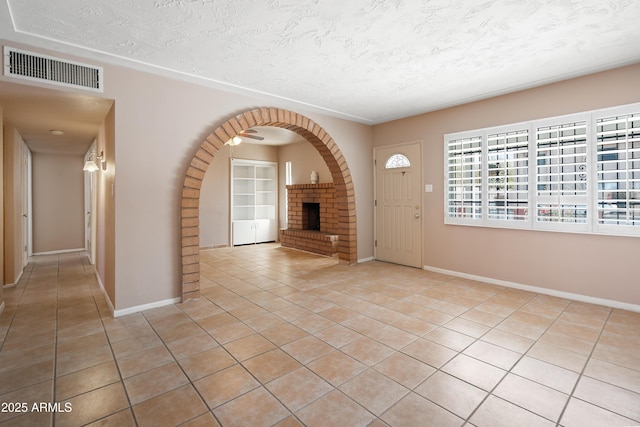 entryway featuring visible vents, a brick fireplace, baseboards, light tile patterned floors, and a textured ceiling