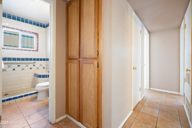 bathroom with baseboards, toilet, a tile shower, and tile patterned flooring